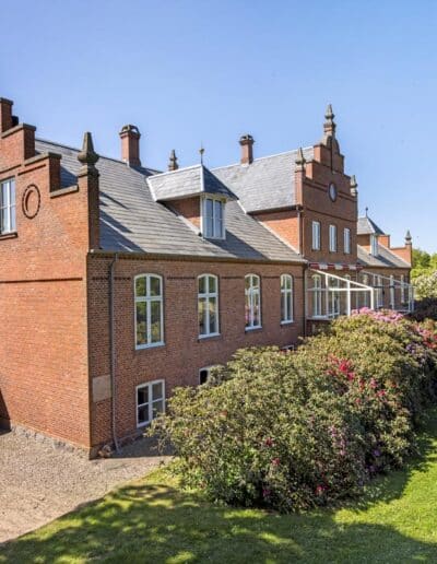 Historisk herregård i røde mursten omgivet af velplejet have og blomstrende buske