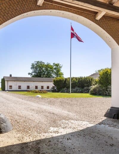 Historisk gårdsplads med Dannebrog fotograferet gennem en stor muret portåbning
