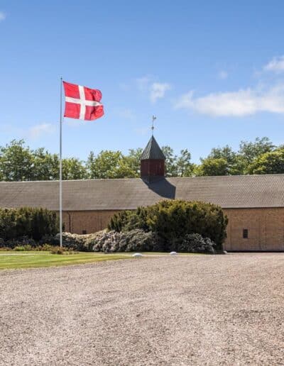 Gårdsplads ved historisk dansk ejendom med Dannebrog, traditionelle bygninger og velplejede udearealer